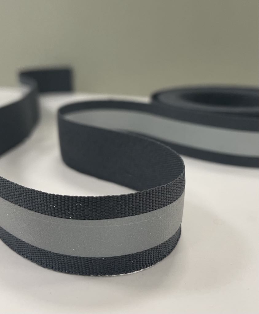 Šviesą atspindinti juostelė, pilka 20 mm Šviesą atspindinti juostelė, pilka 20 mm — siuvimo juostelė | Trys Pelėdos